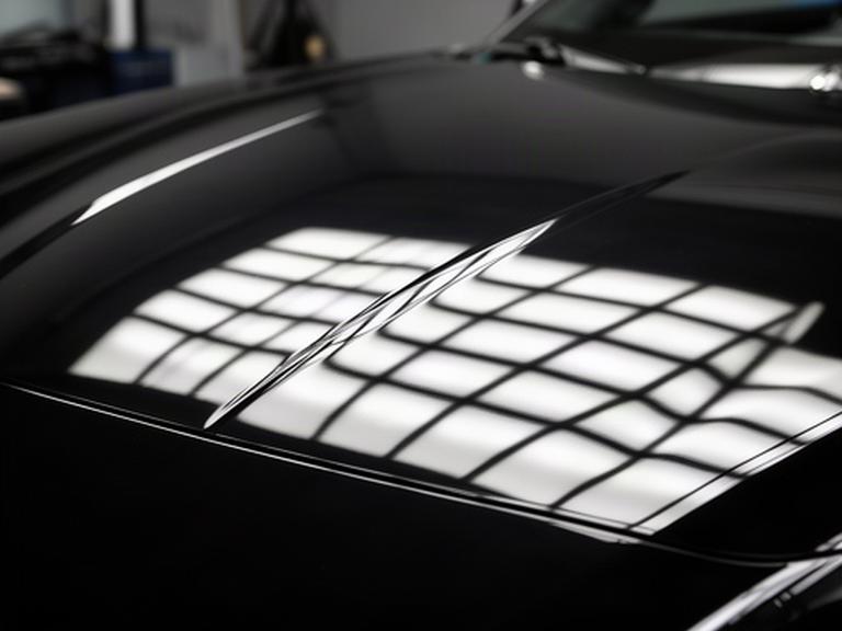 Corrected black car bonnet showing a crisp light-grid reflection and mirror finish